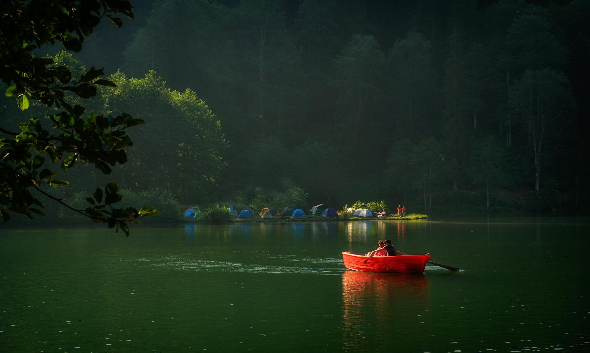 Dwie osoby w czerwonej łodzi płyną po spokojnym zalewie przy campingu