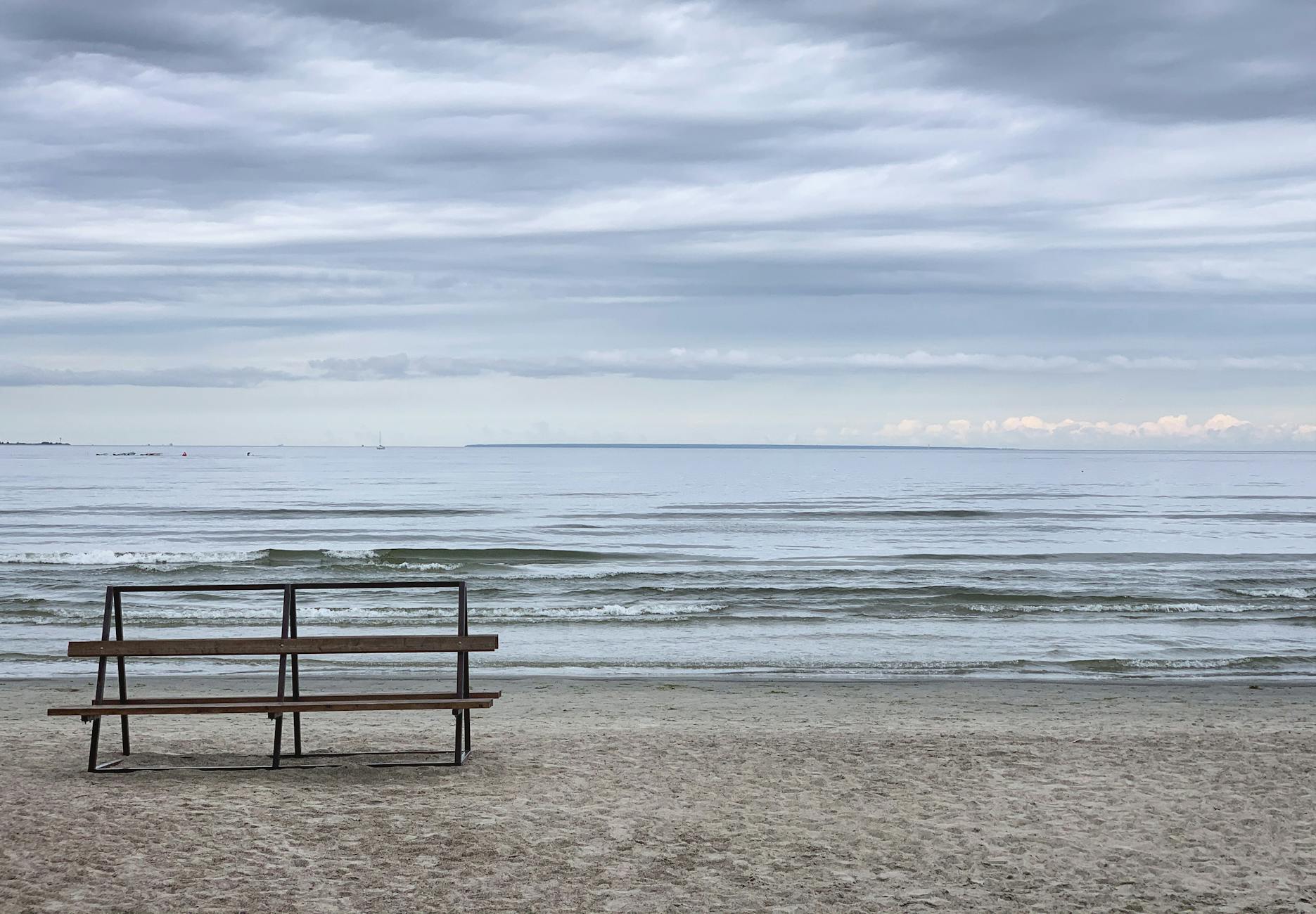 Pusta ławka nad spokojnym morzem Bałtyckim pod pochmurnym niebem