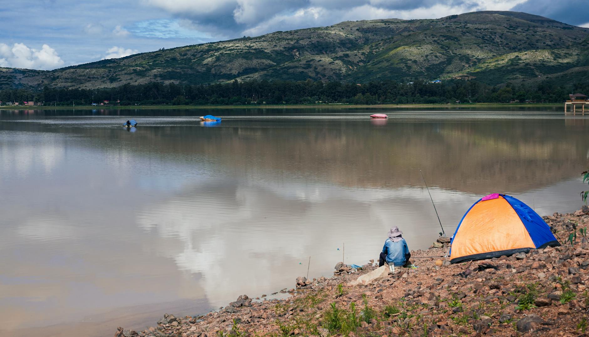 Spokojne pole namiotowe nad zalewem z łodziami i wędkarzami pod chmurami