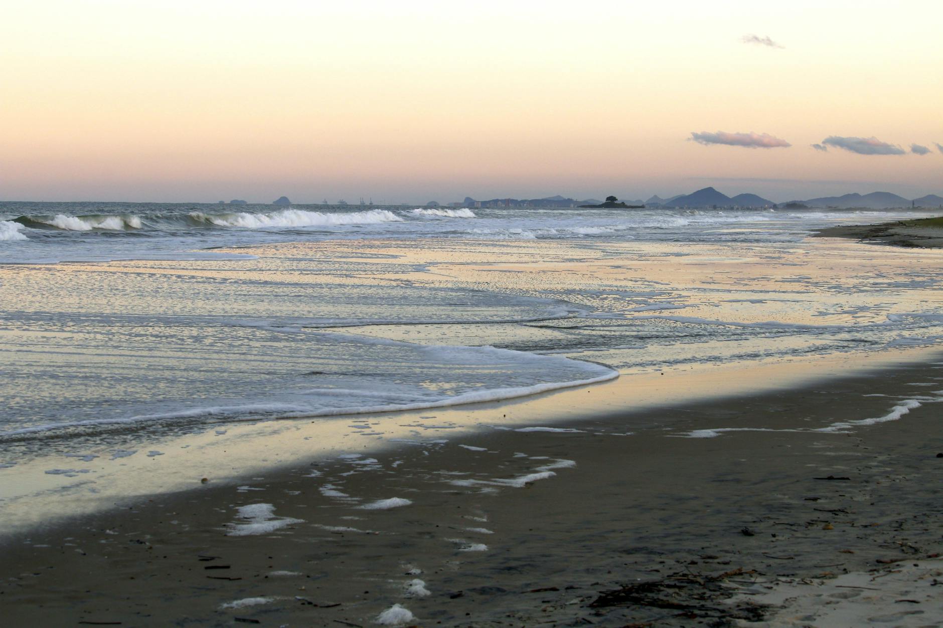 Spokojny zachód słońca nad plażą z łagodnymi falami i górami w tle