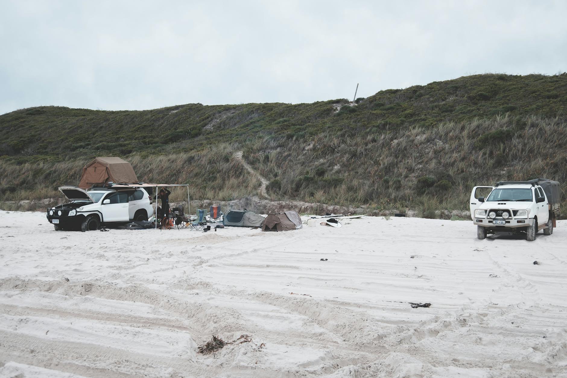 Namioty i terenówki na piaszczystej plaży otoczone zielonymi wzgórzami